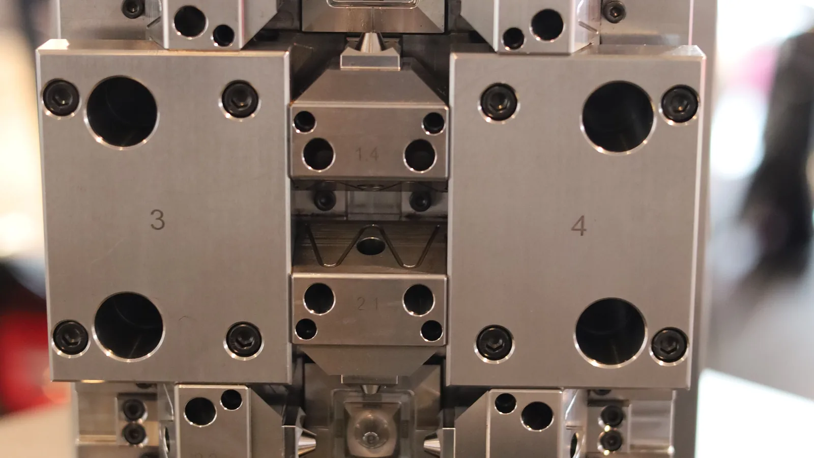 An open multi-component injection mold on a toolroom bench, showing machined cavity and core blocks, inserts, and bolted plates